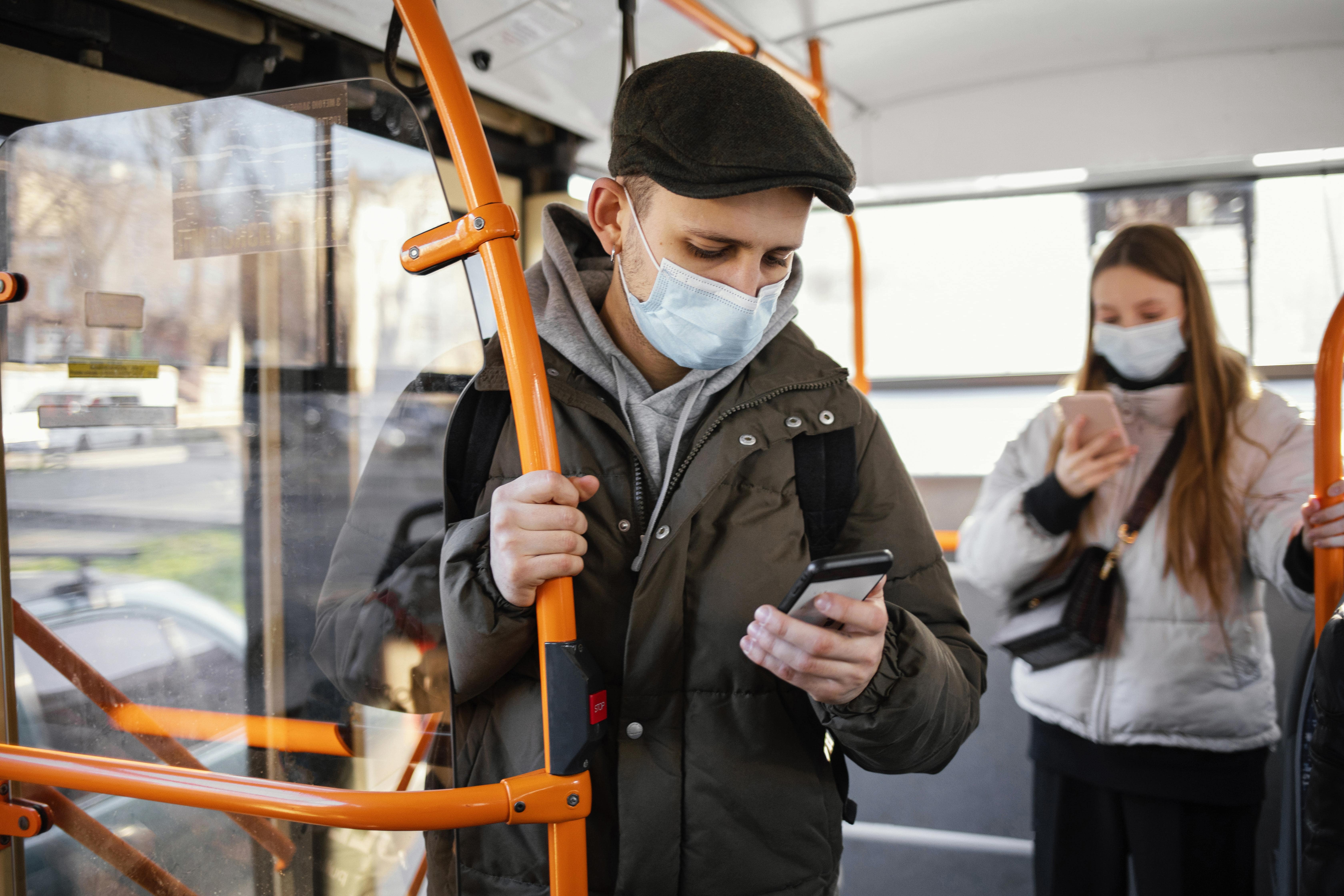 A man on a bus using his smartphone to pre-order food through online food apps, with a woman in the background also engaged on her phone.